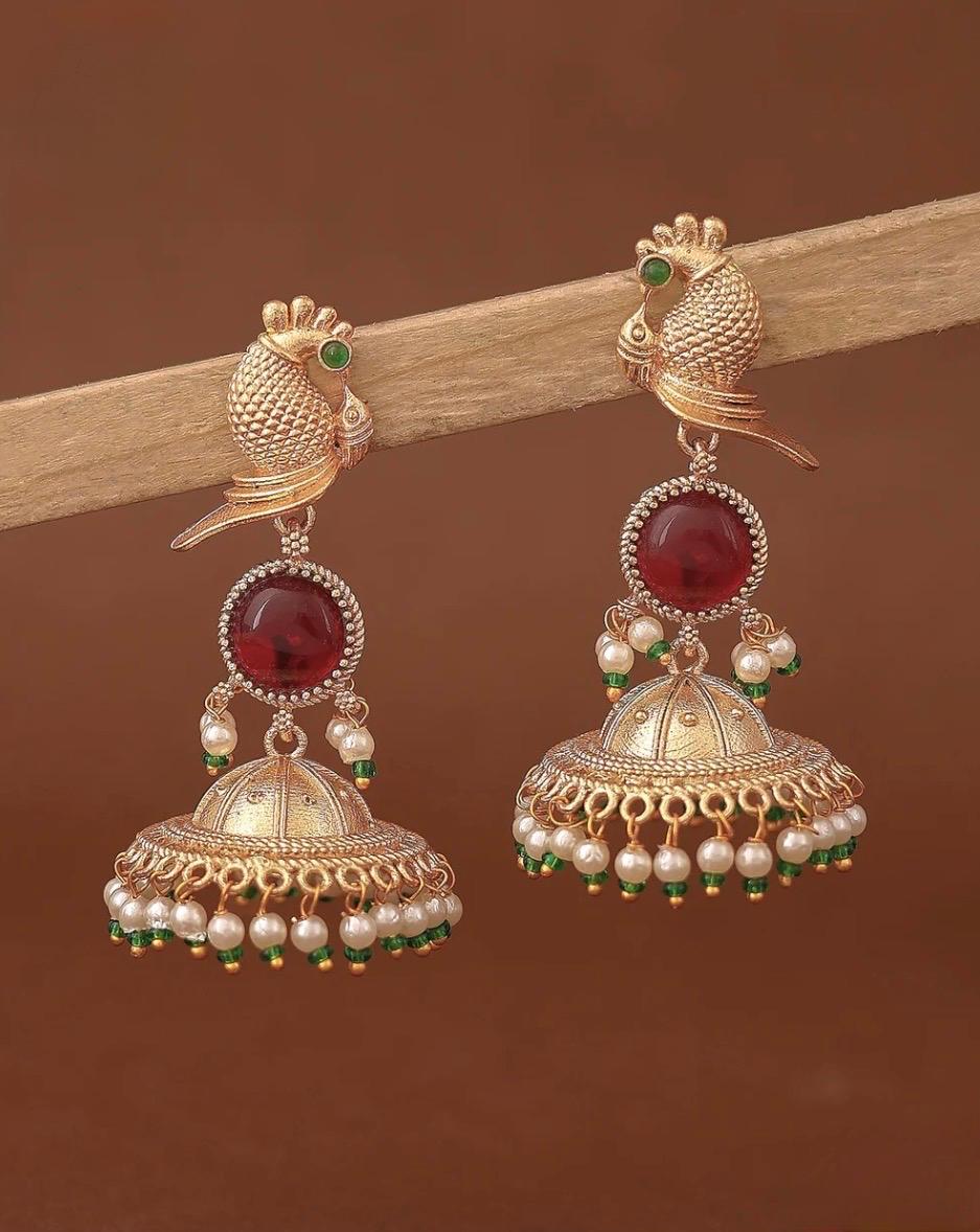 Close up of gold plated Mayur bird jhumka earrings with red stone and pearl drops