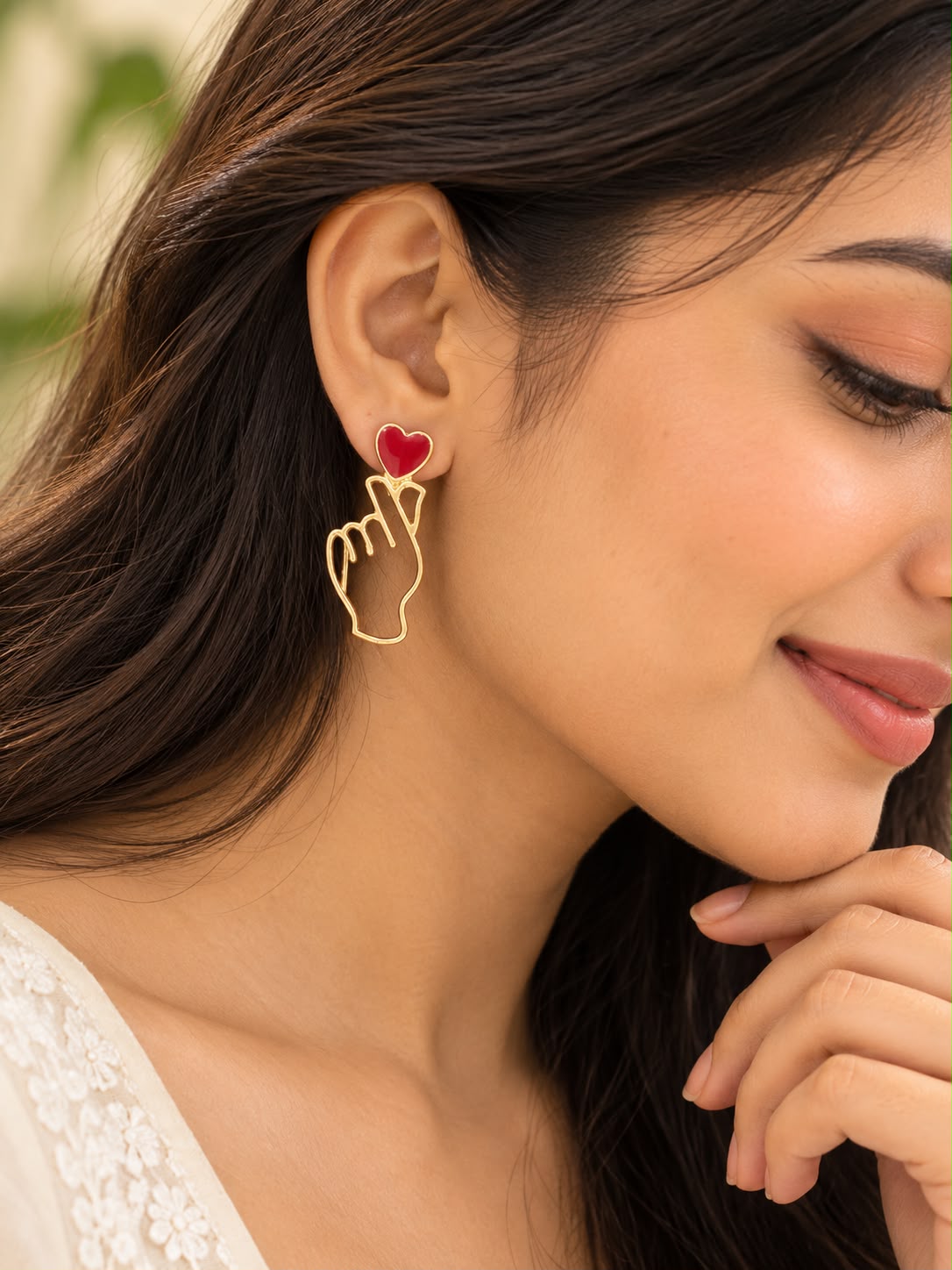 Model wearing Ju-el Love Earrings with red heart stud and open-work gold-tone finger heart silhouette