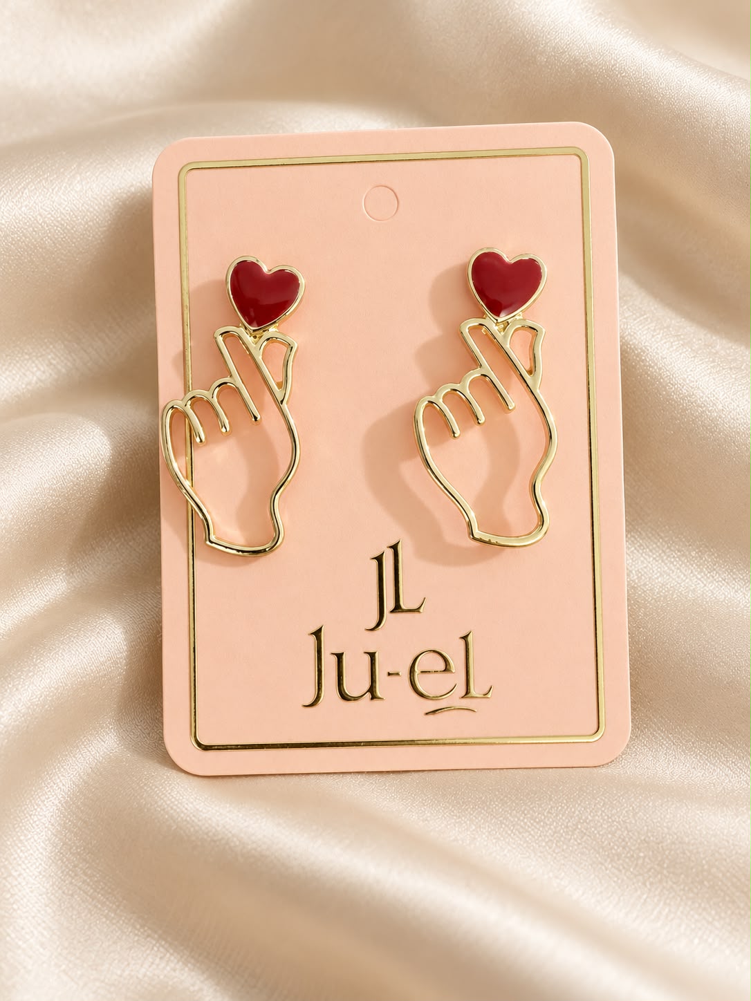 Ju-el Love Earrings featuring heart and finger-heart gold-plated alloy stud design on display card